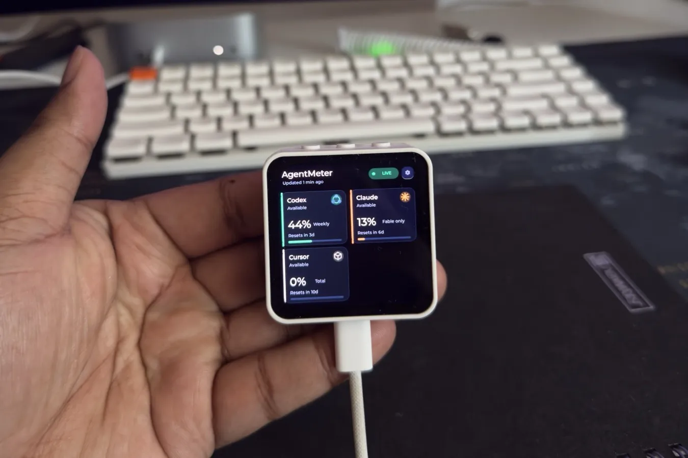 A small round-cornered AMOLED display on a desk showing usage cards